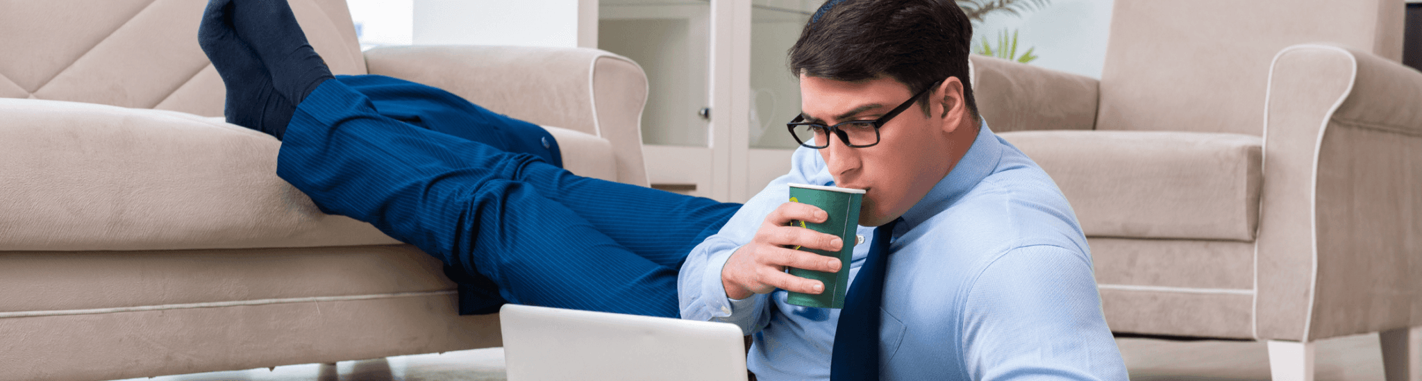 un homme en chaussette devant son PC par terre en train de siroter un jus