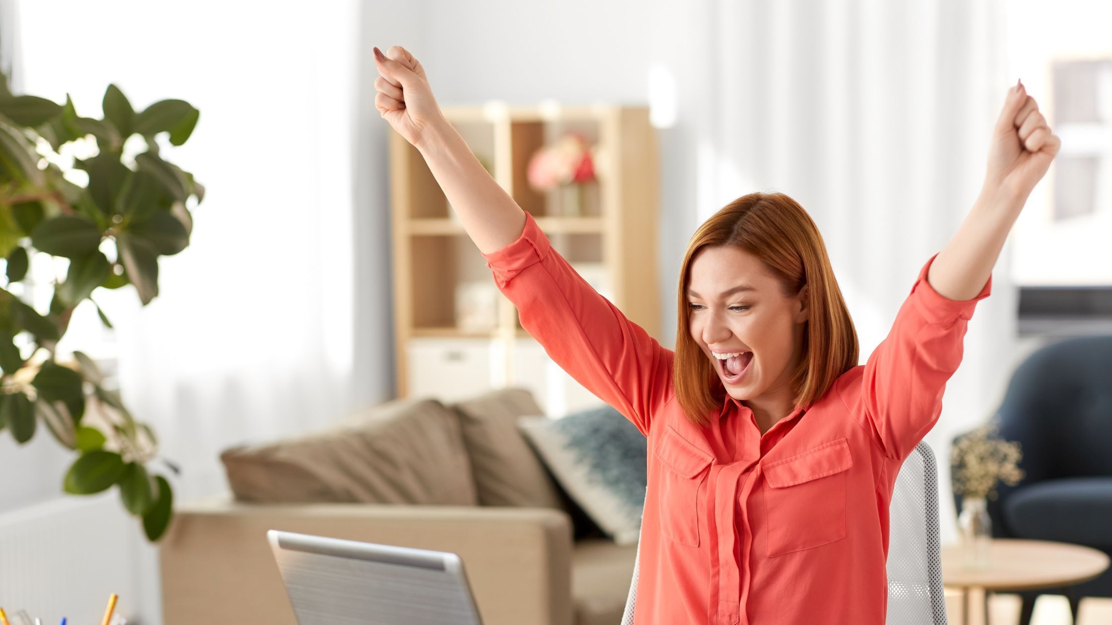 Une femme les bras en l'air de joie devant son écran de PC